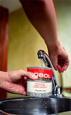 Un fumigène professionnel Dobol est activé sous un robinet d'eau, montrant l'étape d'activation hydro-réactive.