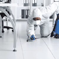 Technicien en tenue de protection traitant un bureau professionnel avec un insecticide anti-cafard.